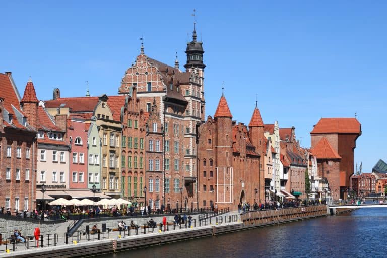 Gdańsk’s historic waterfront along the Motława River, featuring red-brick buildings, ornate facades, and a medieval tower reflected in the calm water.