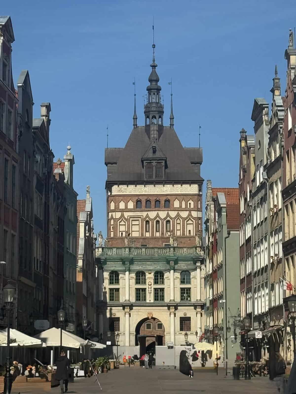 Prison Tower in Gdańsk’s Old Town, with its ornate spire and colorful facades, framed by historic buildings under a bright blue sky.